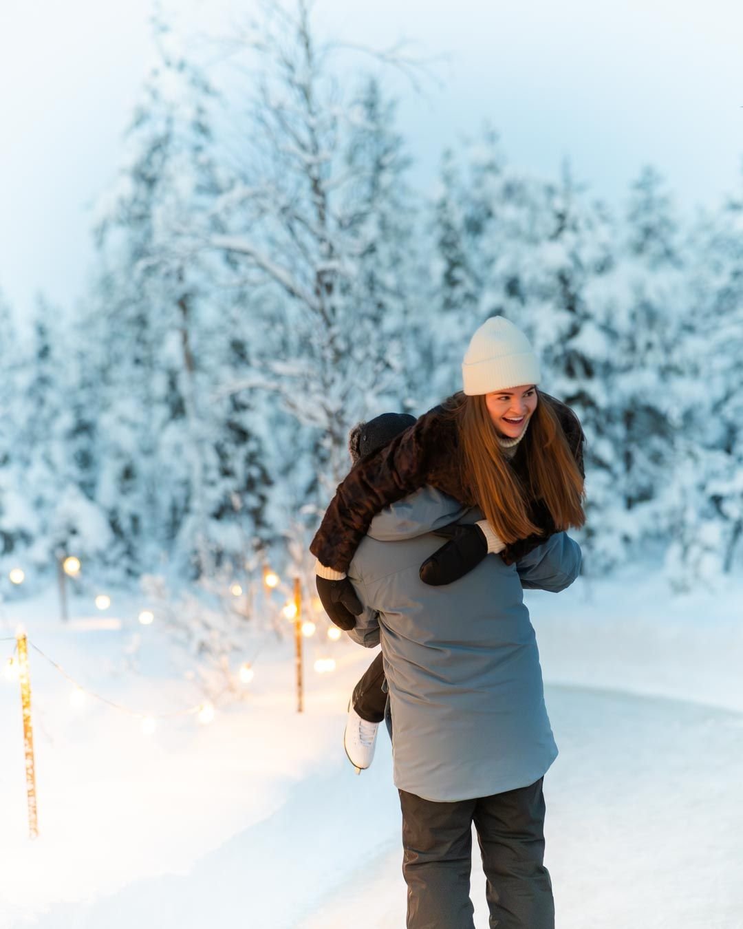 Couple hugging at an outdoor ice rink with string lights in Lapland