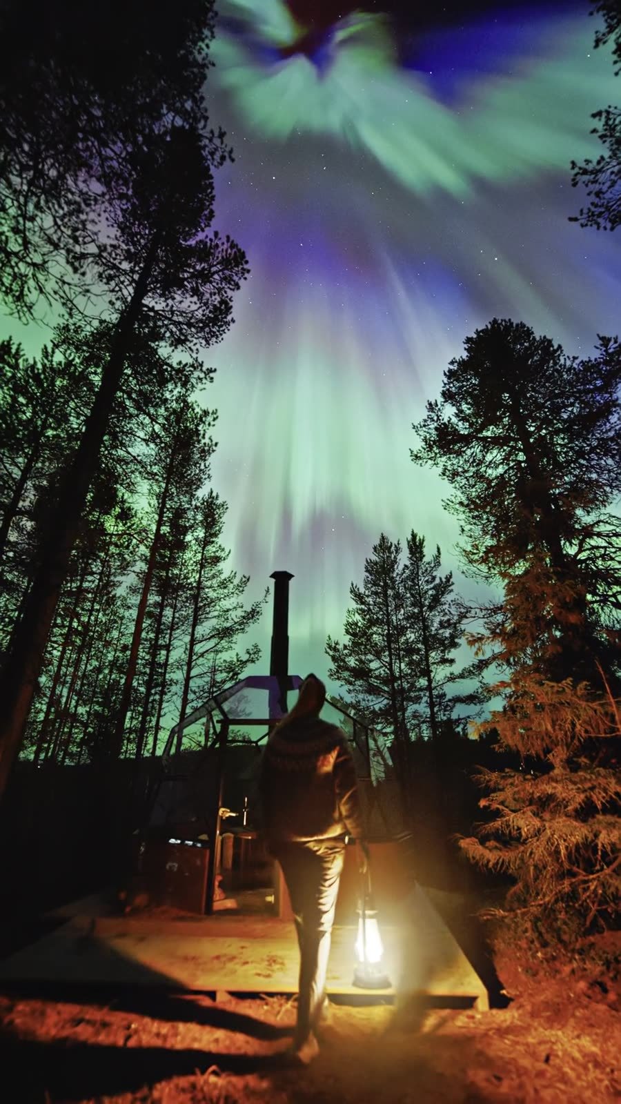 Person with a lantern under the northern lights in Lapland