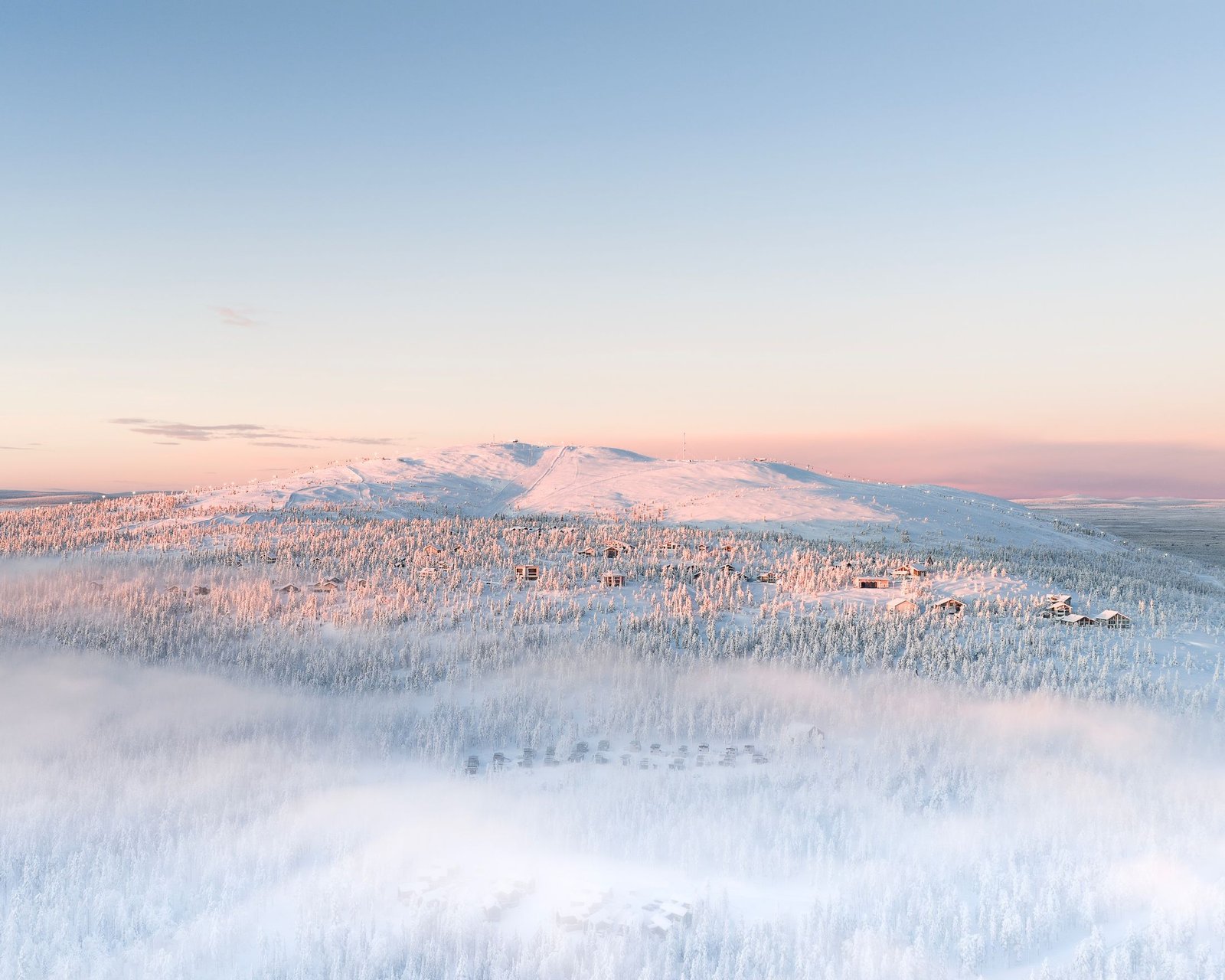 Snow-covered fell and cabins at sunrise in Lapland
